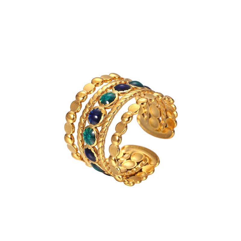 Close up of vibrant green and blue faux gemstones on vintage-style golden wide band ring